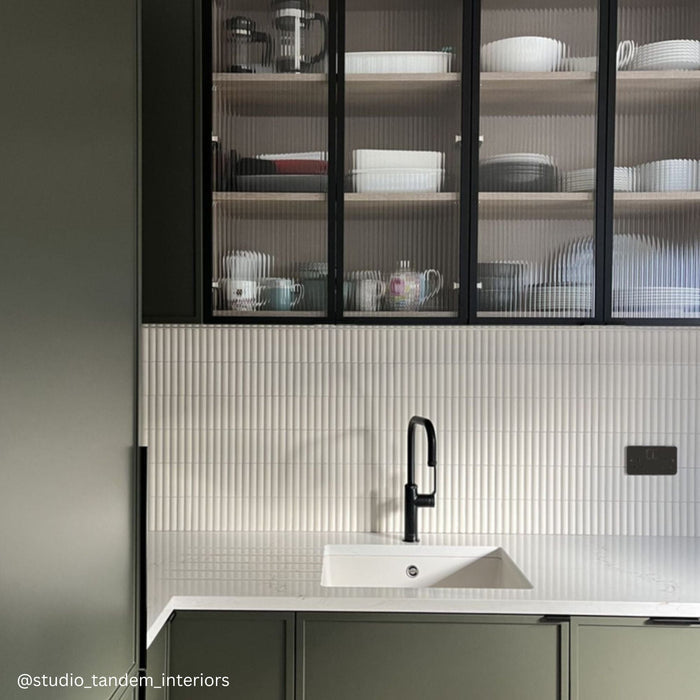 Kitchen with green cupboards and off white fluted wall tiles