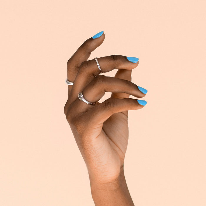 Hand with BKIND Blue Lagoon non-toxic nail polish – vibrant blue manicure in Calgary