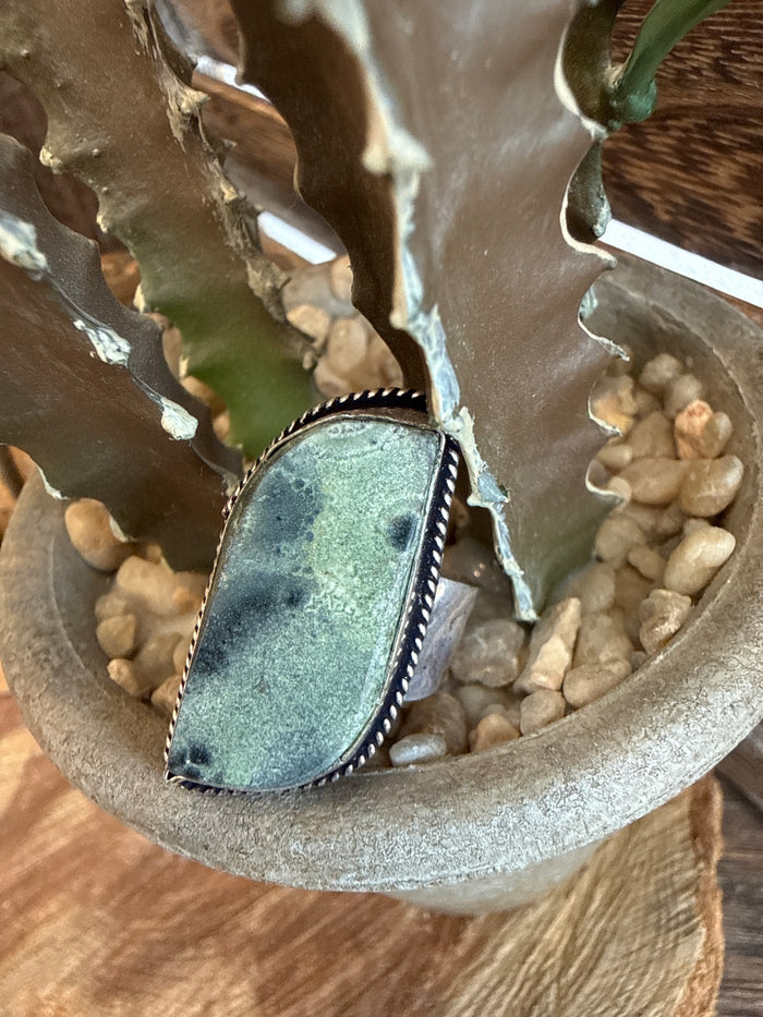 Adjustable ring with oval green stone in silver-toned bezel setting