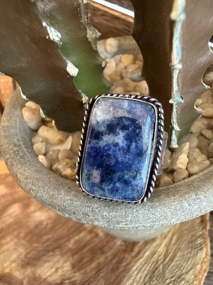 Adjustable ring with oval dark blue stone in silver-toned bezel setting
