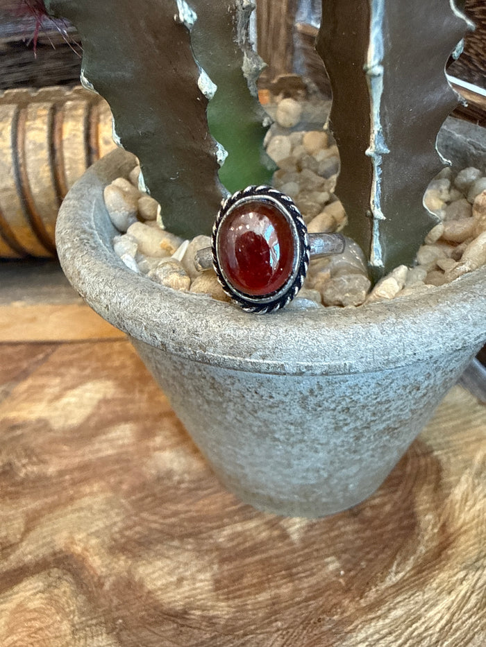 Adjustable brass ring with oval red stone bezel and textured dark border
