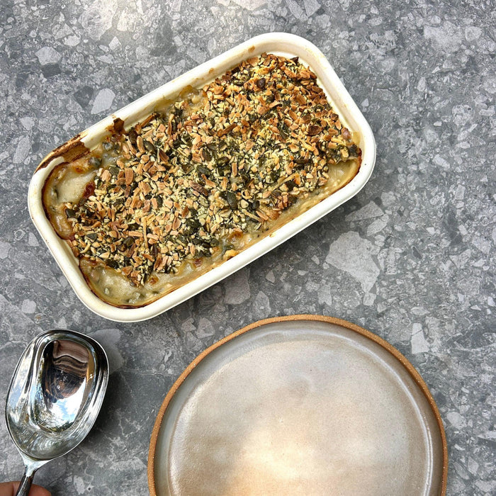Baked dish with gluten free crumb topping on a gray surface with a spoon and plate.