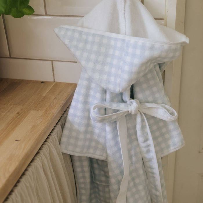 Light blue checkered bathrobe with a white hood and tie, hanging on a wooden surface.
