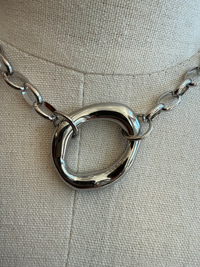 Silver chain necklace close-up with chunky circular ring pendant and metal links