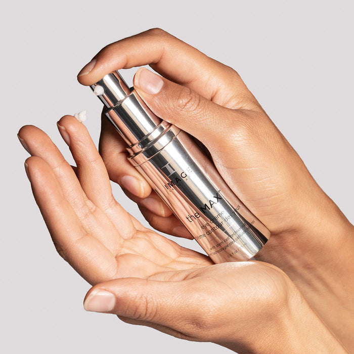 Close-up of hands dispensing a small amount of the MAX™ eye crème | IMAGE Skincare from a sleek silver pump bottle, highlighting skincare and wellness care.