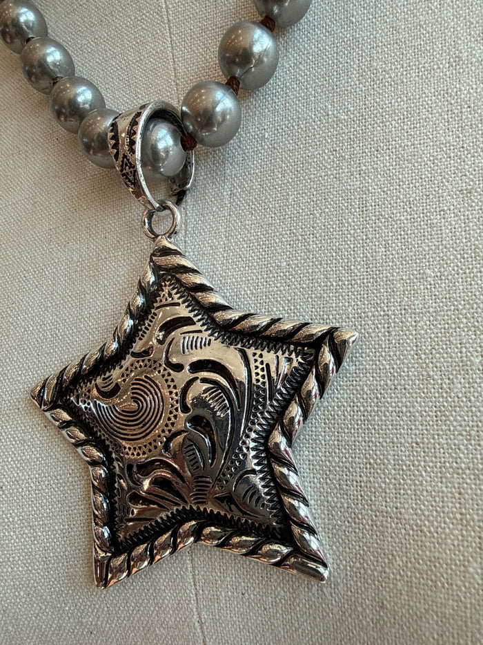 Engraved star pendant with textured metal details on silver beaded necklace