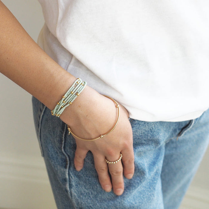 Close-up of a person wearing the Wonder Wrap Bracelet (White Pearl & Gold Multi) | Love You More on their wrist, styled with casual denim and a white shirt.