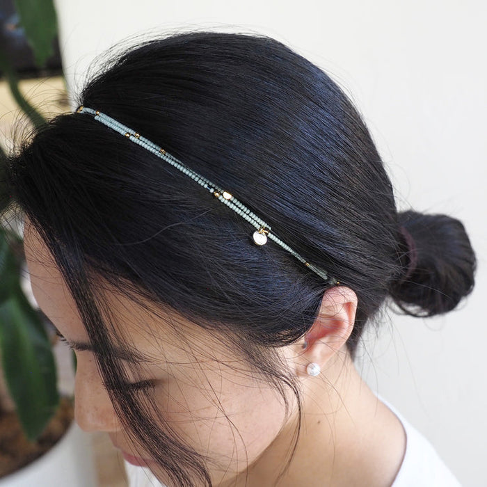 A close-up of a woman wearing the Wonder Wrap Bracelet (White Pearl & Gold Multi) | Love You More as a delicate headband, showcasing white pearls and gold accents in her dark hair.